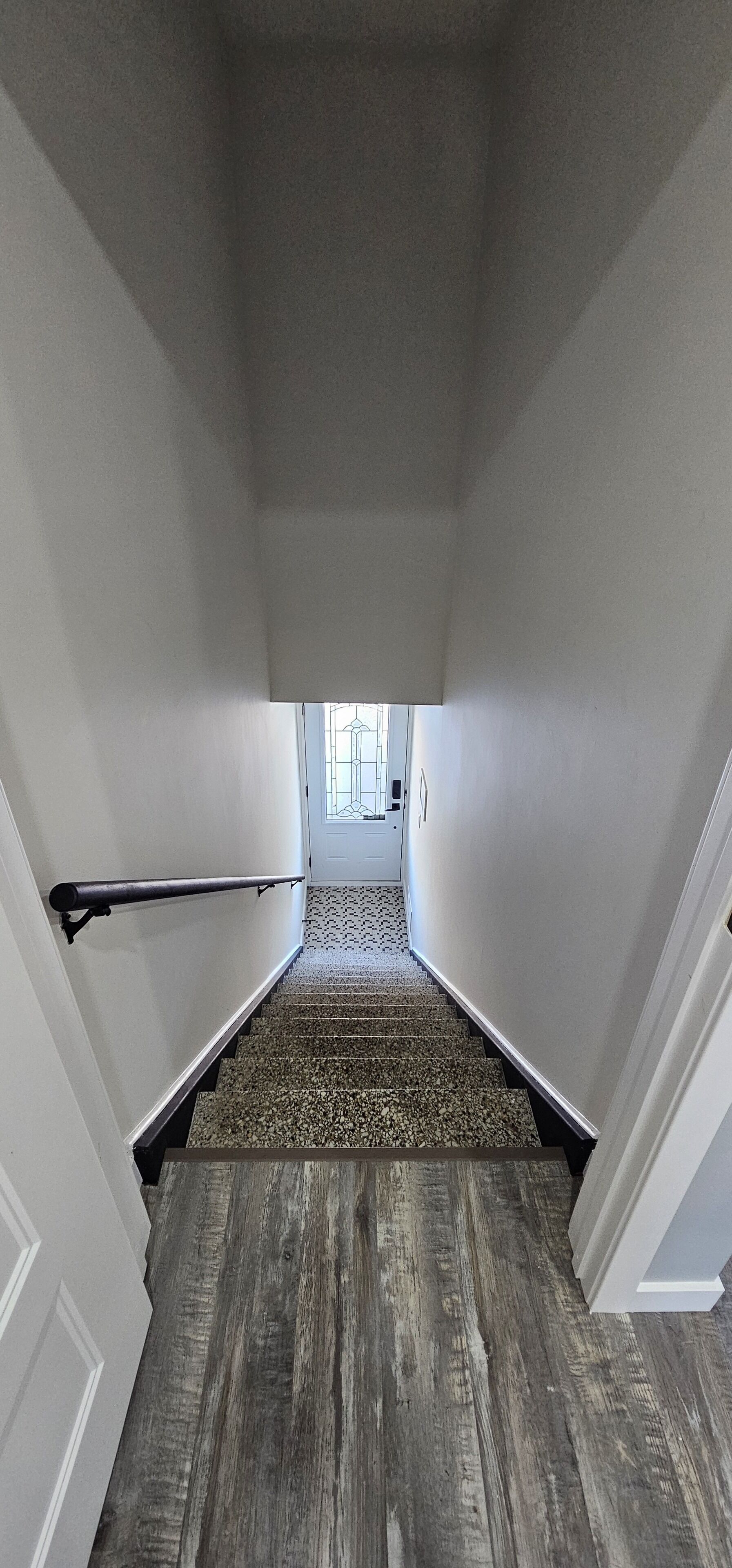 A staircase with a wooden finish, white walls, and a metal handrail.