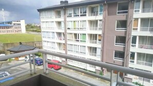 En bygning med flere etager, altaner, parkeringsplads og en idrætsbane i baggrunden.