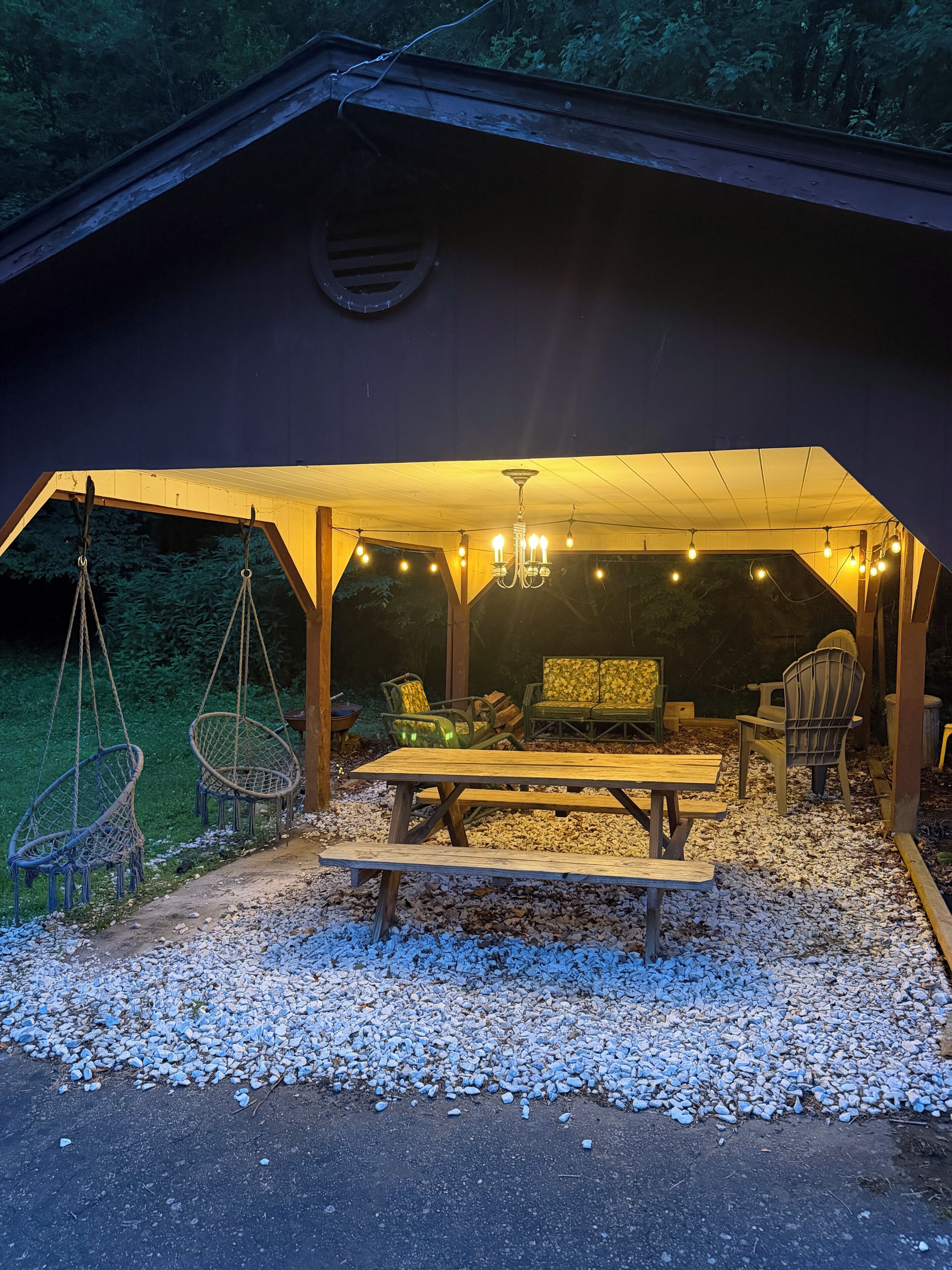 An outdoor seating area with a wooden table and chairs, a hanging chair, and a string of lights.