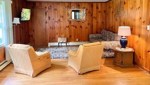 A room with wooden paneling, a sofa, two armchairs, a small table with a lamp, and a television on the wall. - Creekside Rural Retreat in Beautiful Ashe County
 (Lansing)