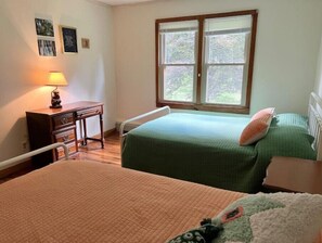 A bedroom with two beds, a desk, and a window with a view of trees.