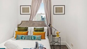 A neatly arranged bedroom with a bed, pillows, a bedside table with a lamp, and two framed pictures on the wall. - Cosy Apartment 5 guests - 3 beds + 1 sofa bed Lewisham, London (London)