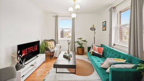 A modern living room with a green sofa, a flat-screen TV, a coffee table, and a potted plant. - Cosy Apartment 5 guests - 3 beds + 1 sofa bed Lewisham, London (London)