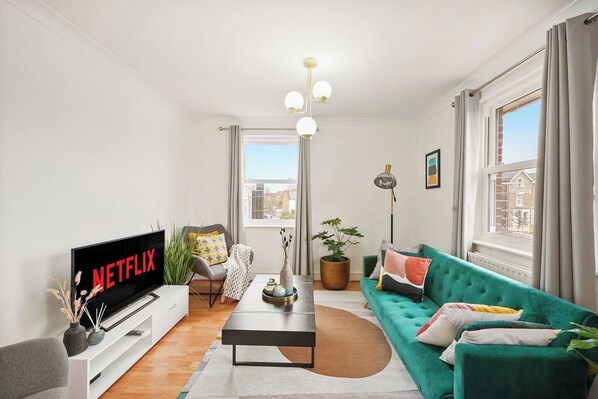 Una sala de estar moderna con un sofá verde, un televisor de pantalla plana, una mesa de centro y una planta en maceta.
