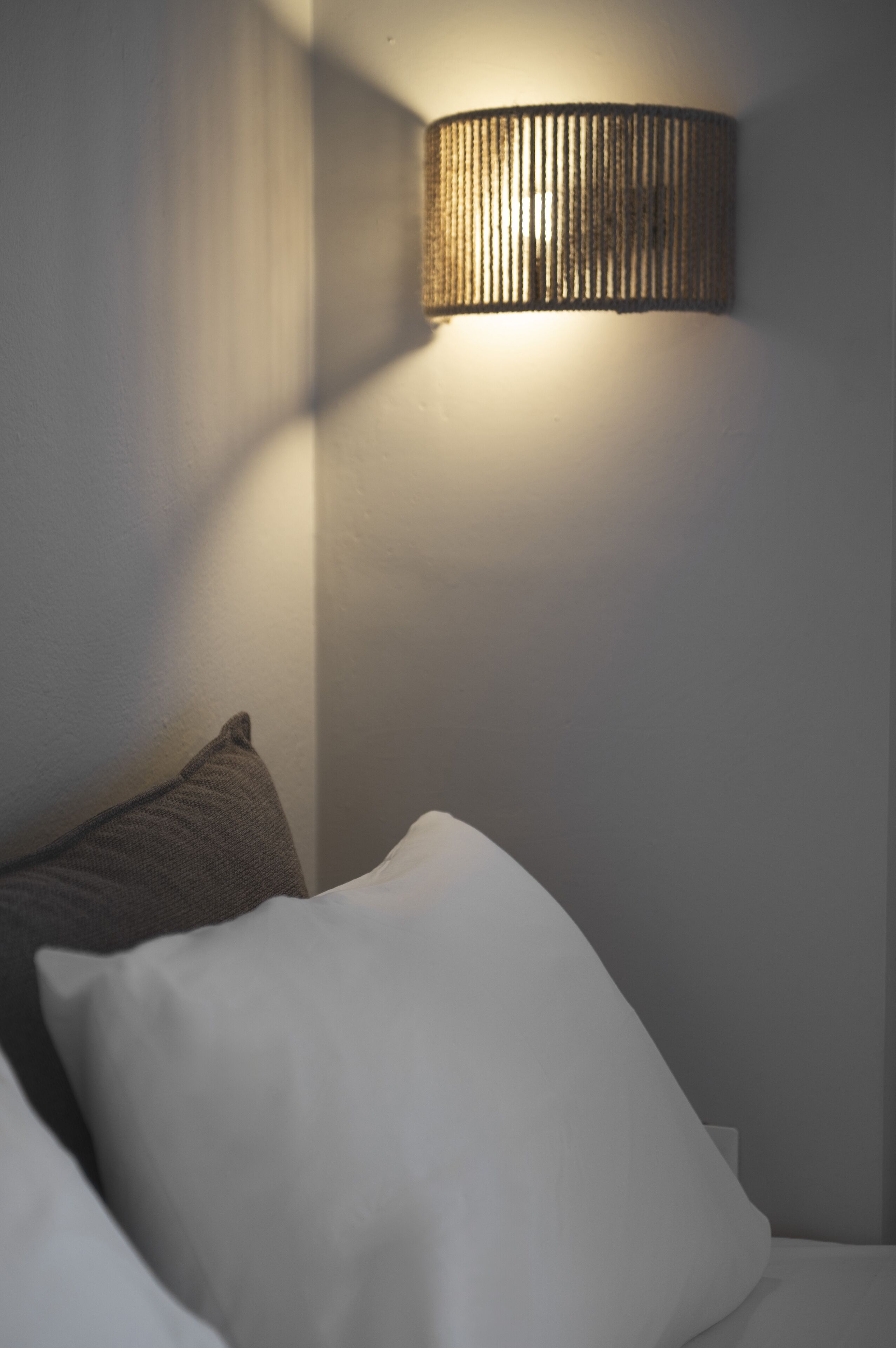 A bedroom with a bed, pillows, and a wall-mounted lamp.