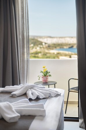 A hotel room with a bed, a small table with a potted plant, and a view of the sea and landscape. - Casa di Demezzo (Sitia)