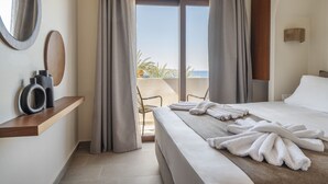A hotel room with a bed, a small table, a chair, and a view of the sea through large windows. - Casa di Demezzo (Sitia)