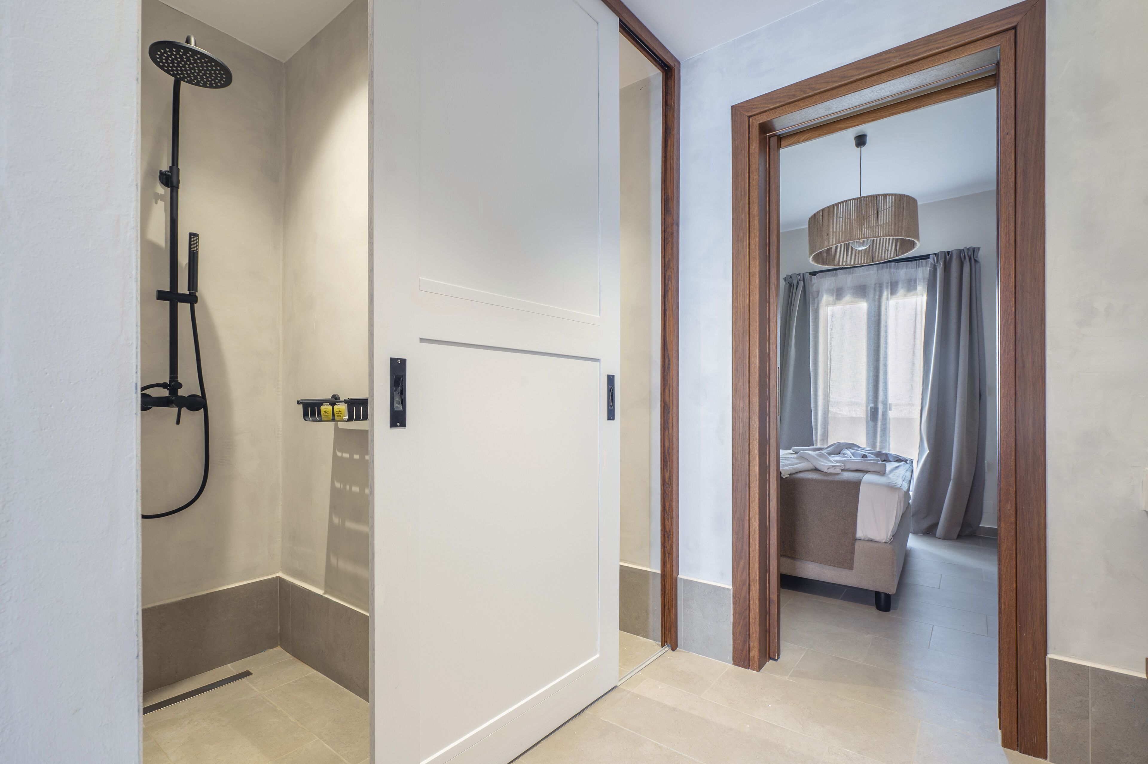 Une salle de bain moderne équipée d’une douche, de toilettes et d’un lavabo. Une porte en bois donne accès à une chambre à coucher qui comprend un lit et une fenêtre.