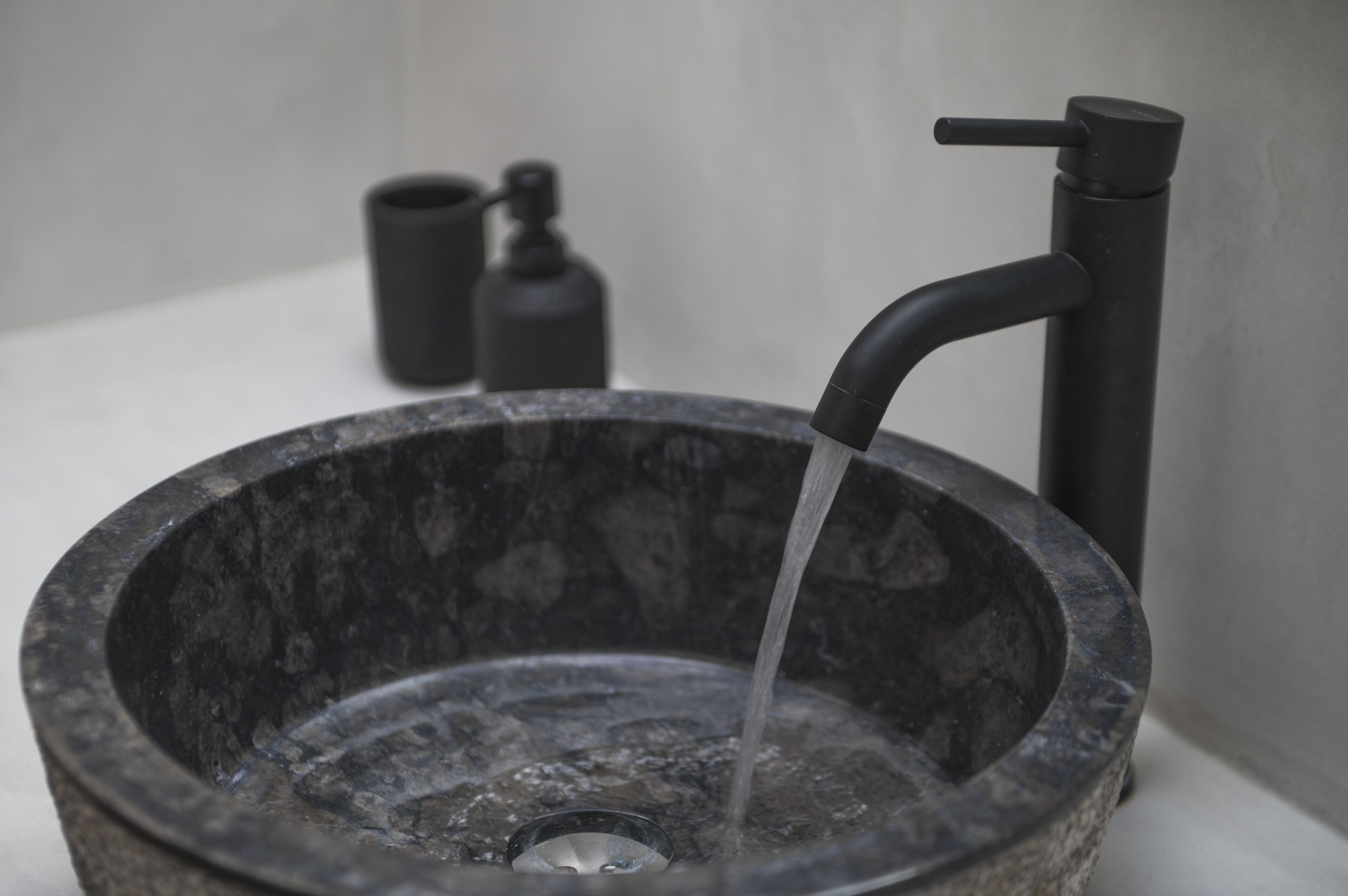 Un évier en pierre, doté d’un robinet moderne, avec un distributeur de savon en arrière-plan.