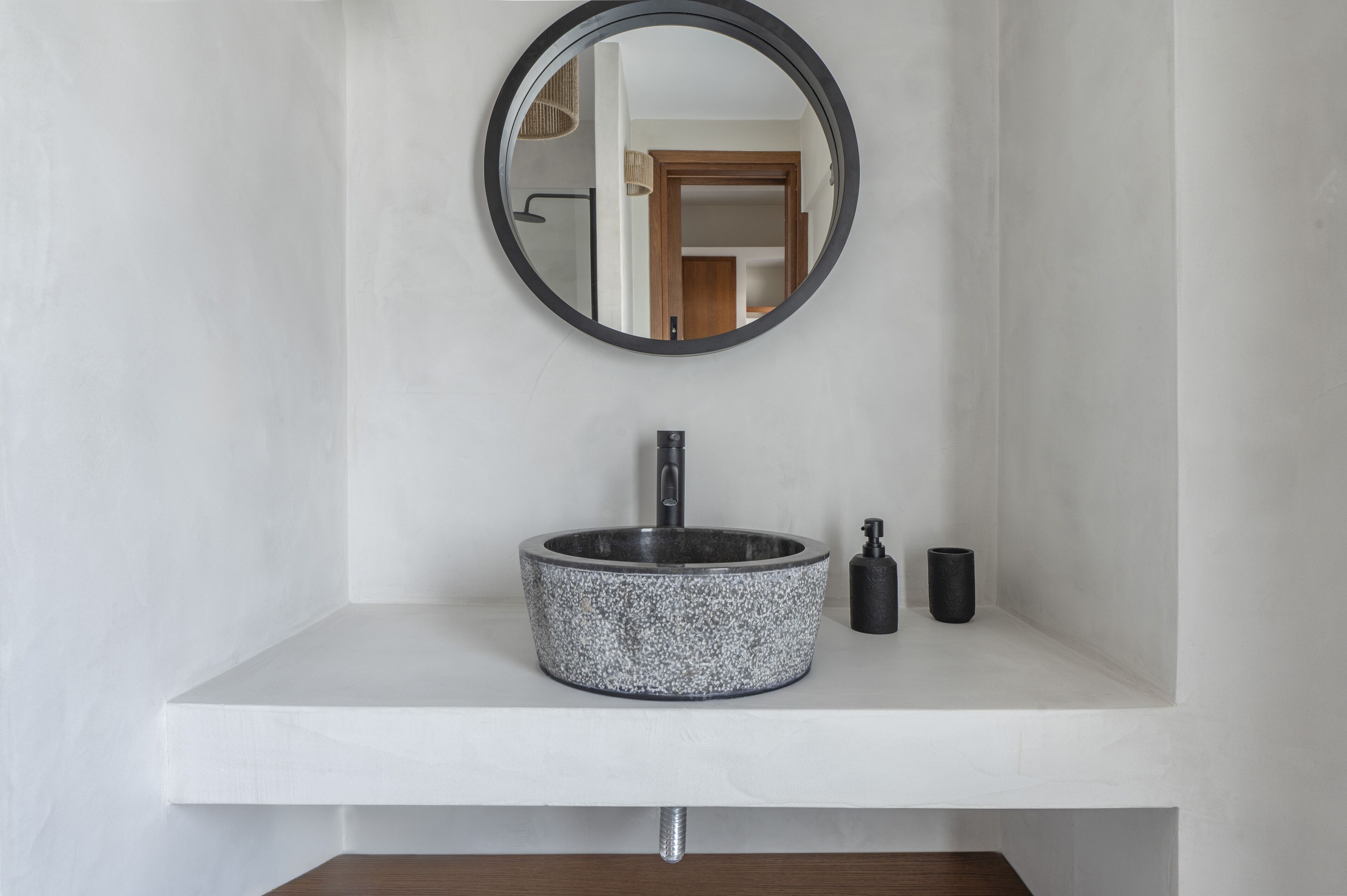 A bathroom with a round mirror, a speckled sink, and a small black soap dispenser.