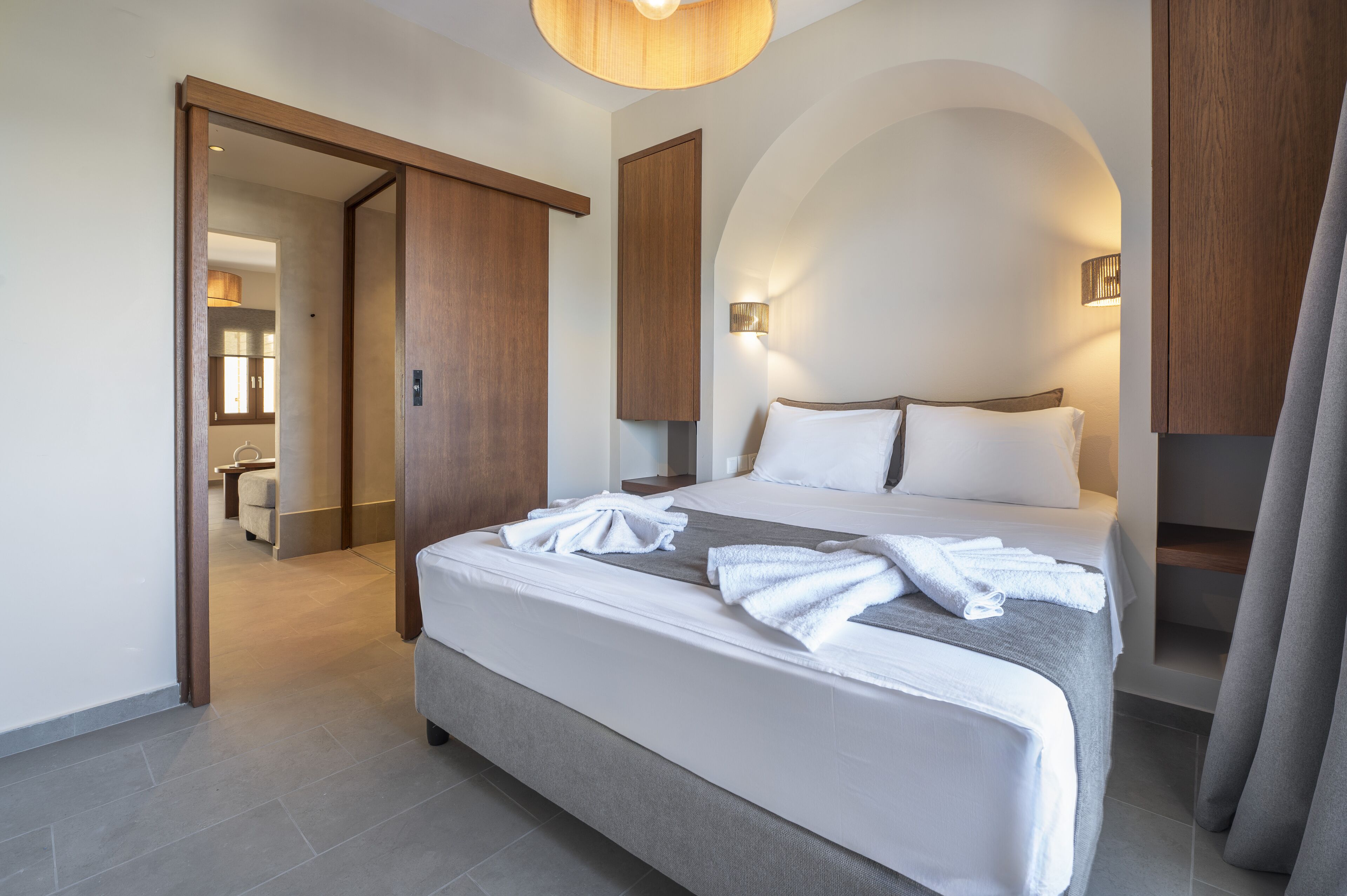 Une chambre d’hôtel moderne dotée d’un grand lit, d’un dressing et d’une salle de bain visible à travers une porte ouverte.