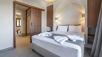 Une chambre d’hôtel moderne dotée d’un grand lit, d’un dressing et d’une salle de bain visible à travers une porte ouverte.