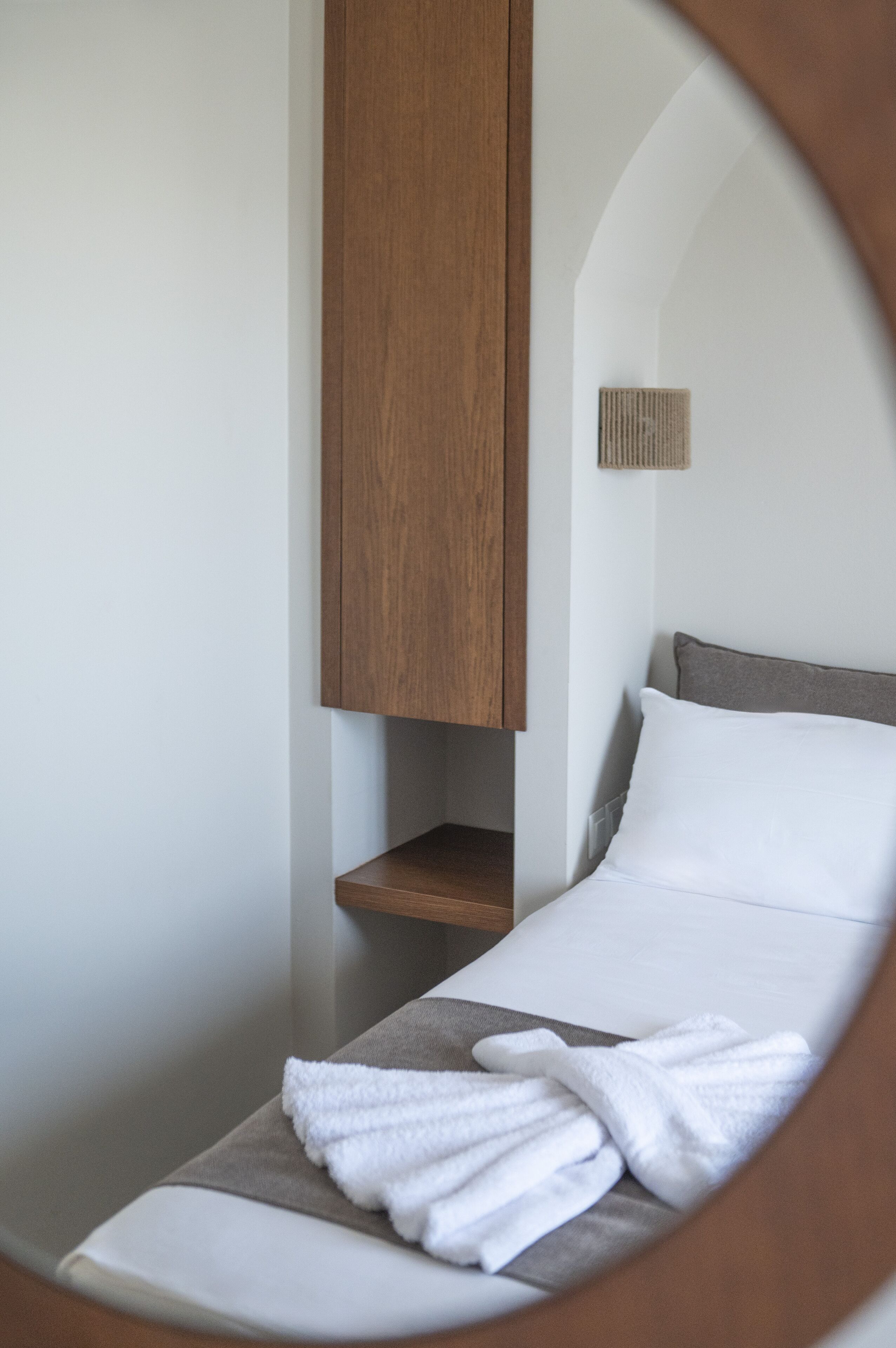 A small, private room with a bed, a wooden cabinet, and a towel on the bed.