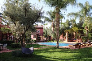 A pool area with lounge chairs, a hanging chair, and a building with a red facade. - Villa DALIA (Ghmate)