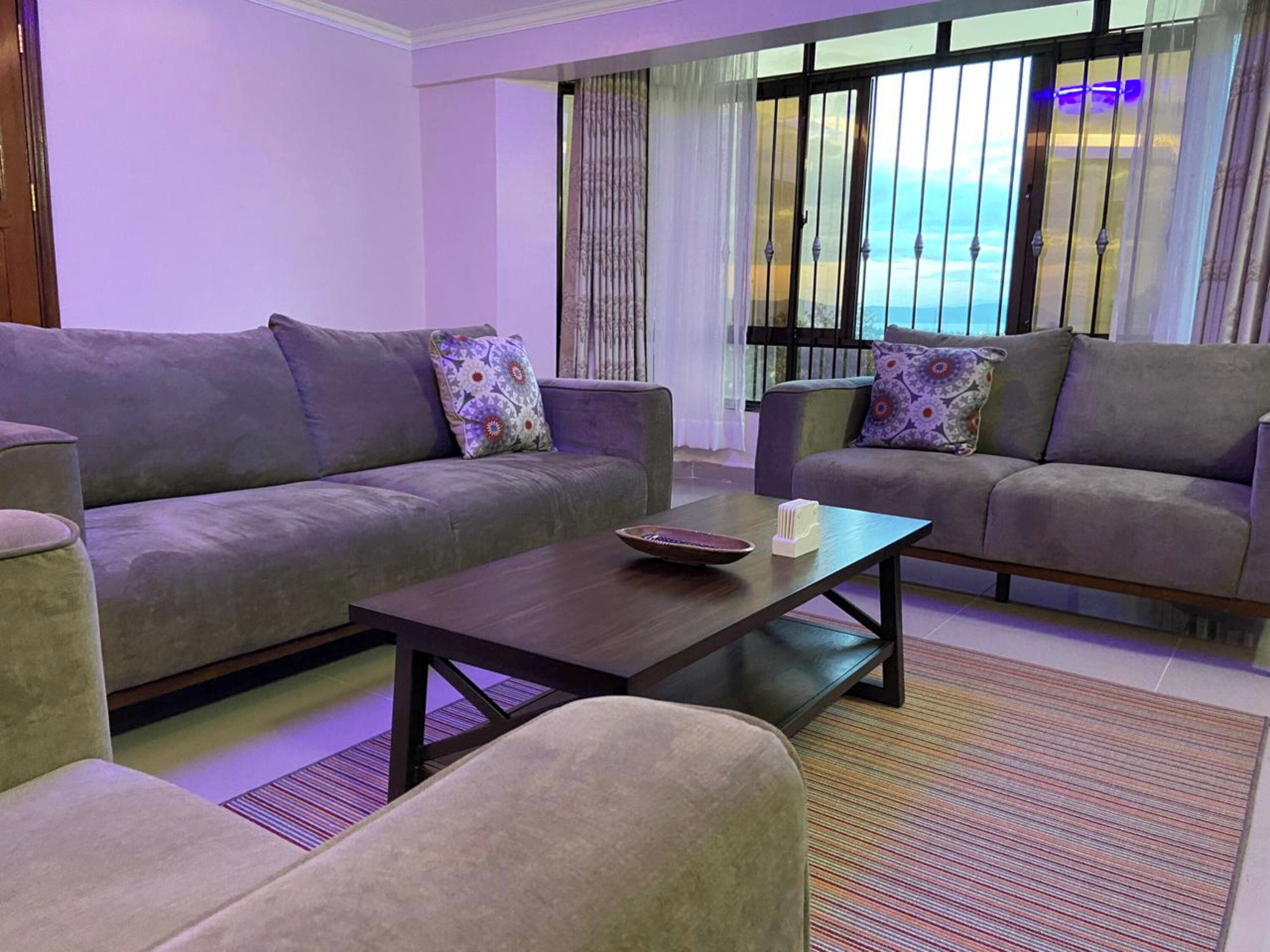 A modern living room with two grey sofas, a coffee table, and a view of the outdoors through large windows.