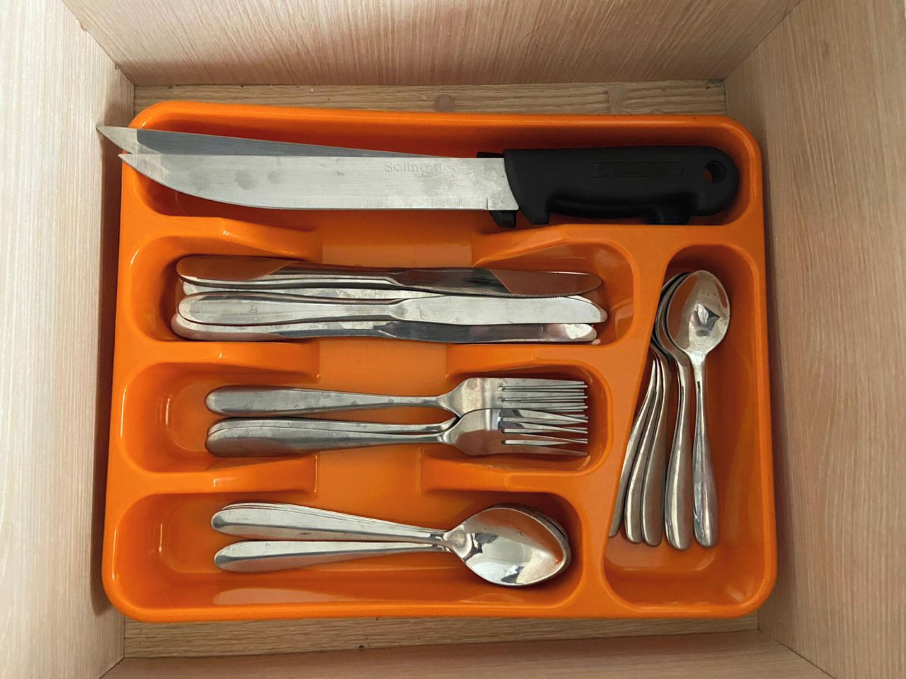 A drawer containing a knife, forks, spoons, and a spoon rest.