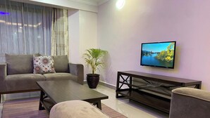 A modern living room with a sofa, a coffee table, a TV, and a potted plant. - Midtown B61 Apartment (Nakuru)