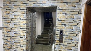 A modern elevator with a stone wall design, a metal handrail, and a digital display showing the number 5. - Midtown B61 Apartment (Nakuru)