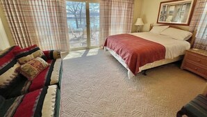 Une chambre à coucher comprenant un lit, un ventilateur de plafond, une table de chevet, une lampe, un canapé et une vue sur l’extérieur grâce à une porte-fenêtre coulissante.