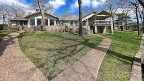 Une maison à deux étages avec une façade en pierre, un patio couvert et une pelouse bien entretenue.