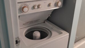 Vista frontal de uma máquina de lavar compacta, branca, com abertura frontal, painel de controle com botões e um tambor pequeno e circular.