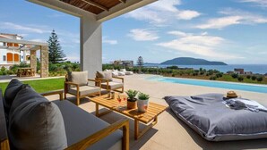 A modern outdoor lounge area with a pool, seating, and a view of the sea and mountains.