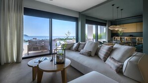 A modern living room with a large sofa, a round coffee table, and a view of the sea through large windows.