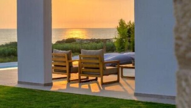 A modern outdoor seating area with a view of the sunset over the ocean.