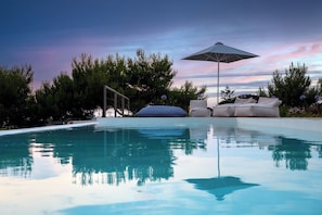 A swimming pool with a clear reflection, surrounded by greenery and a sunset sky. - Villa with private infinity pool, sea view & sunset. Nobus Villas 1 (Marathopoli)