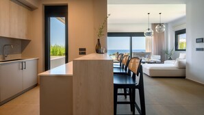 Eine moderne Küche mit Kochinsel, ein Essbereich mit Sofa und Sesseln sowie Meerblick.