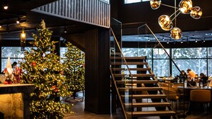 Ein modernes Interieur mit einer Holztreppe, einem Weihnachtsbaum und einem Essbereich mit Personen.