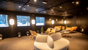 Ein stilvoller Lounge-Bereich mit einer runden weißen Couch, Holzstühlen und Stehlampen. Große Fenster bieten Blick auf eine verschneite Landschaft.