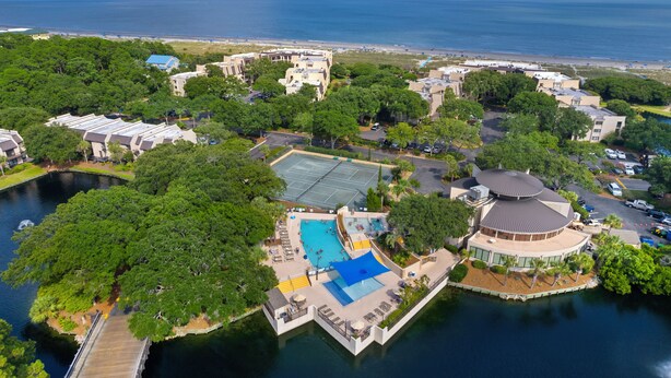 An aerial view of a resort with a central swimming pool, a dock, and a beach in the background. - Surfside Hideaway (Hilton Head Island)