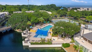 An aerial view of a resort with a large swimming pool surrounded by lush greenery and a body of water. - Surfside Hideaway (Hilton Head Island)