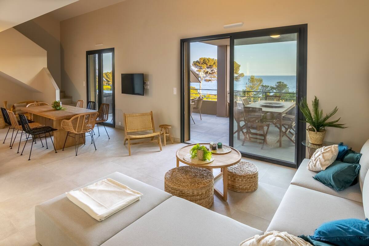 Uma sala de estar moderna com um sofá, uma mesa de jantar com cadeiras e uma varanda com vista para o mar.