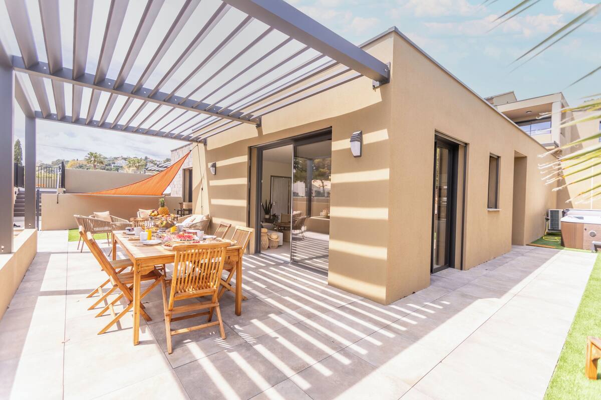 Uma área moderna para refeições ao ar livre, com pérgola, mesa posta para quatro pessoas e vista do edifício vizinho.