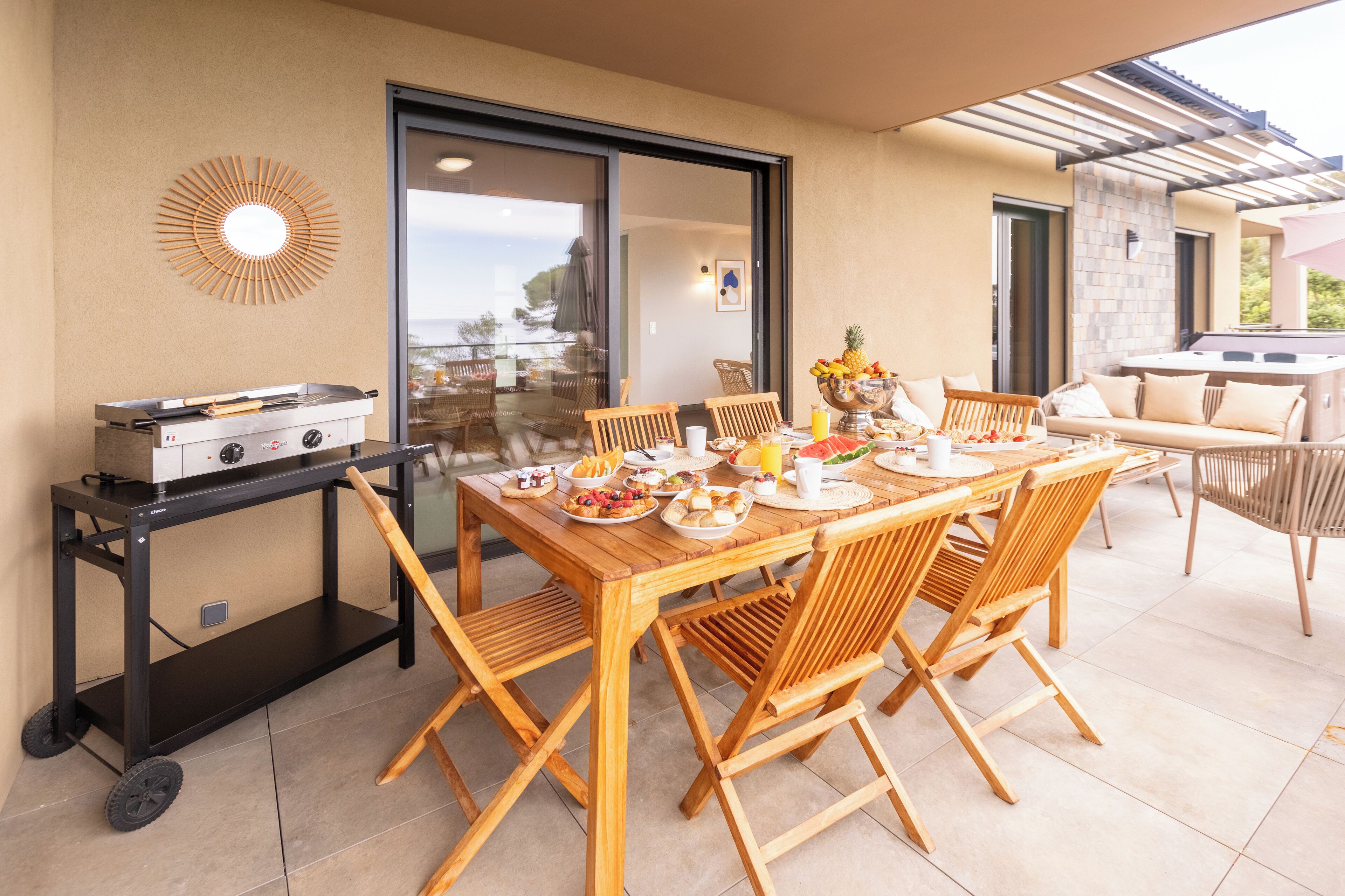 Eine Terrasse mit Frühstückstisch, Grill und Gartenmöbeln.