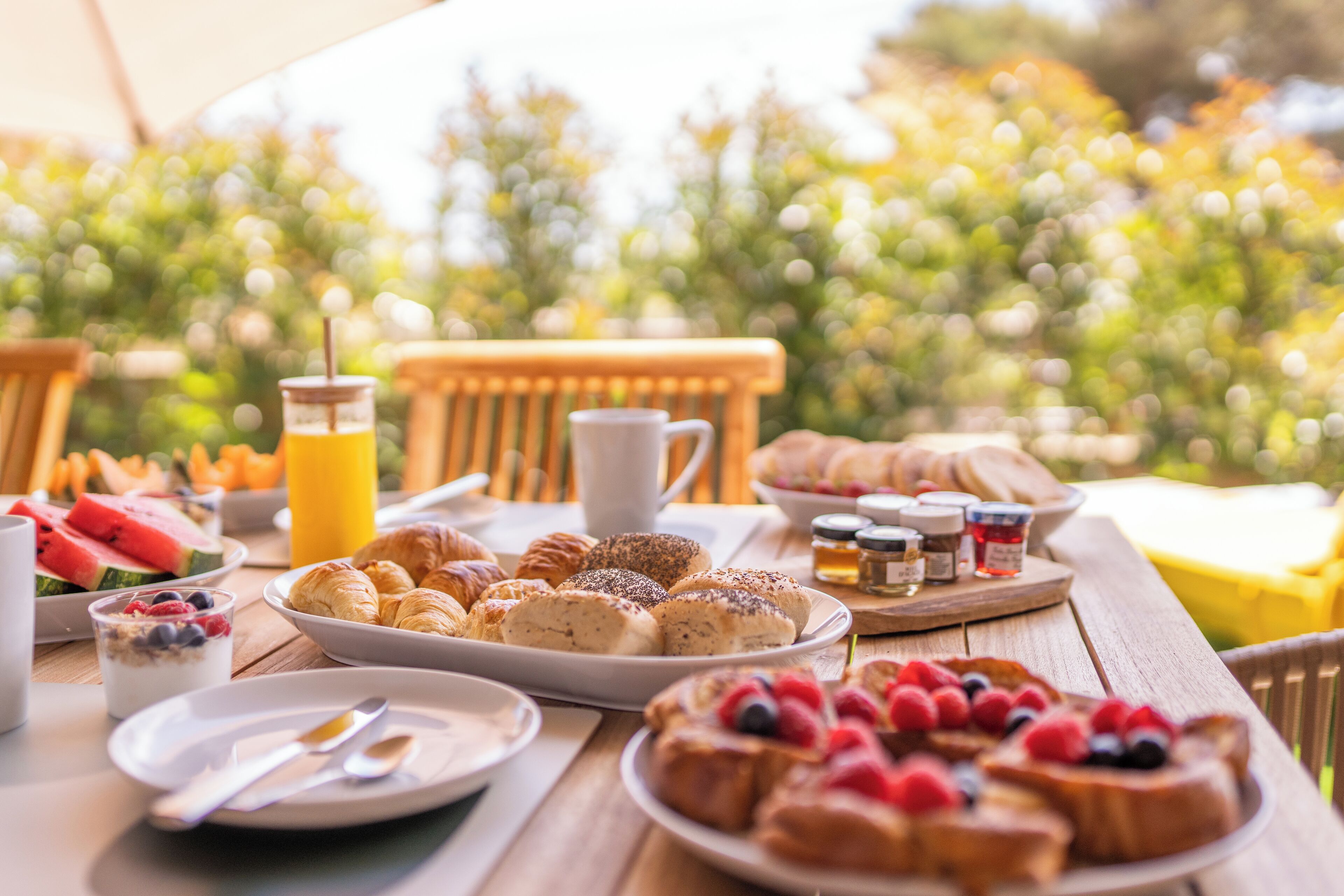 A breakfast table with various foods and drinks, including pastries, fruits, and a glass of orange juice.
