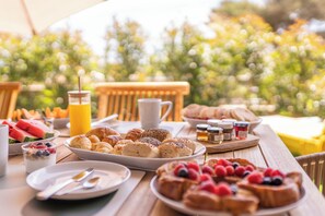 Et morgenbord med forskellige spiser og drikkevarer, blandt andet bagværk, frugt og et glas appelsinjuice.