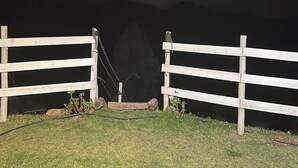 Une clôture en bois avec un portail donnant sur un paysage sombre où l’on aperçoit la lune.