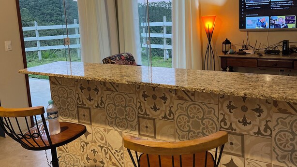 Une cuisine avec un coin bar, des carreaux décoratifs, des luminaires suspendus et un téléviseur diffusant les actualités.