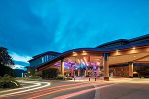 A modern hotel with a curved entrance, large columns, and a well-lit facade.
