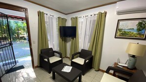 A room with two black armchairs, a small table, a white sofa, a TV mounted on the wall, and a painting. - Manuel Antonio a 100 Metros del mar (Quepos)