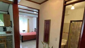 A hallway with a bed, a potted plant, and a bathroom visible through an open door.