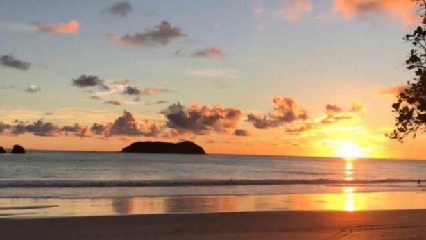A sunset over a beach with calm waters and distant landforms. - Manuel Antonio a 100 Metros del mar (Quepos)