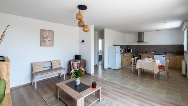 A modern living room with a sofa, coffee table, and a dining area with chairs and a table. A kitchen is visible in the background with a refrigerator and microwave. - Logis de la Perruche - Maison avec terrasses (Montreuil-Bellay)