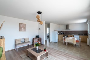 A modern living room with a sofa, coffee table, and a dining area with chairs and a table. A kitchen is visible in the background with a refrigerator and microwave. - Logis de la Perruche - Maison avec terrasses (Montreuil-Bellay)