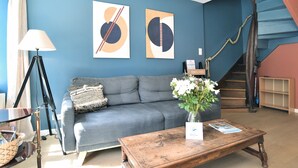 A living room with a blue wall, a grey sofa, a wooden coffee table, and a staircase. - Mézange Bleue - Près du canal d'Ille et Rance (Lanvallay)