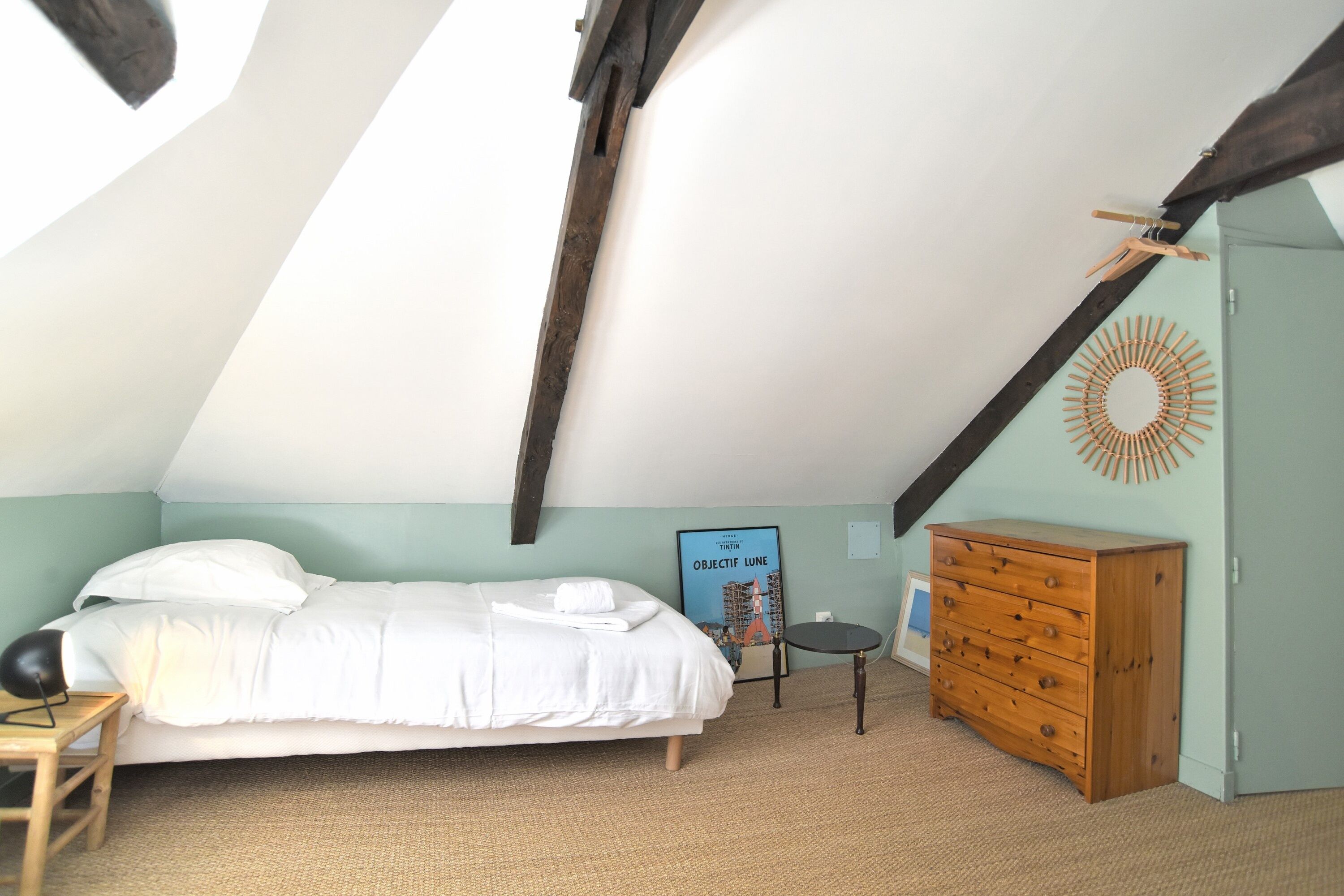Een slaapkamer met een bed, een houten dressoir en een poster aan de muur.