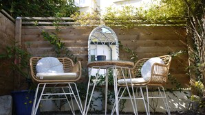 Une clôture en bois, deux fauteuils en osier avec des coussins, une petite table et un miroir à cadre métallique.